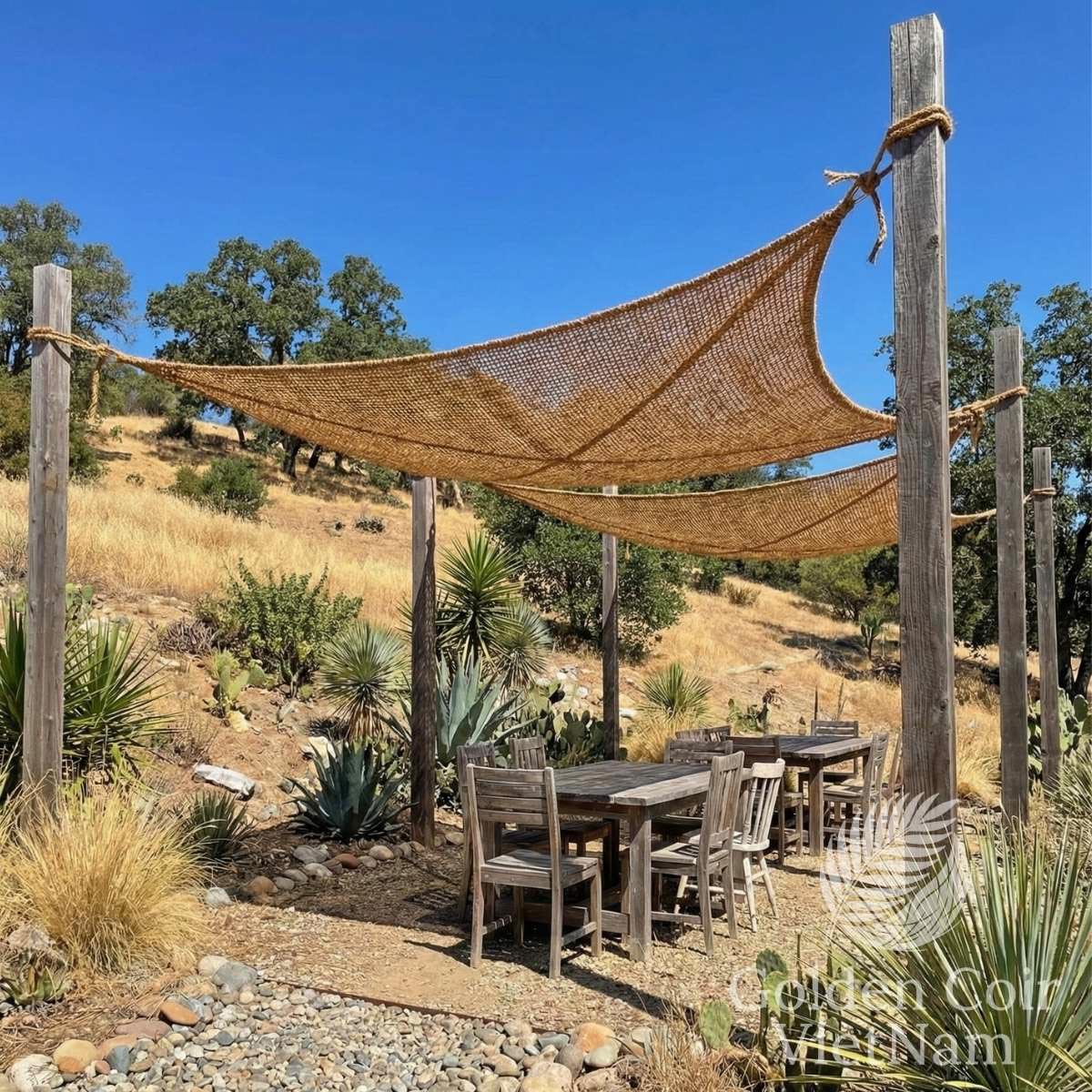 Natural coir shade sail installed with a hyperbolic paraboloid twist, tensioned between wooden posts to provide breathable outdoor shade over a rustic dining area