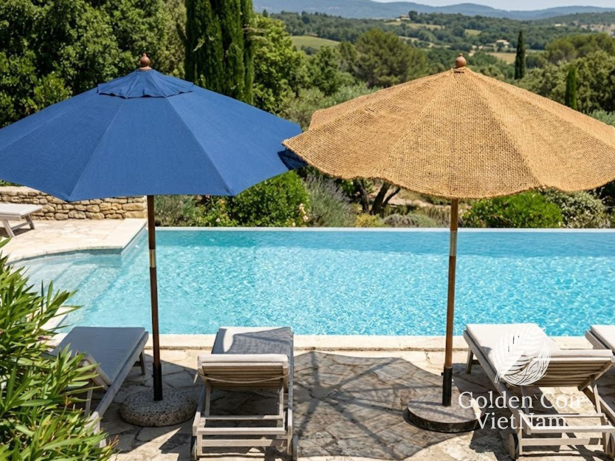 Poolside comparison of a blue synthetic fabric patio umbrella and a natural coir (coconut fiber) parasol shading lounge chairs.