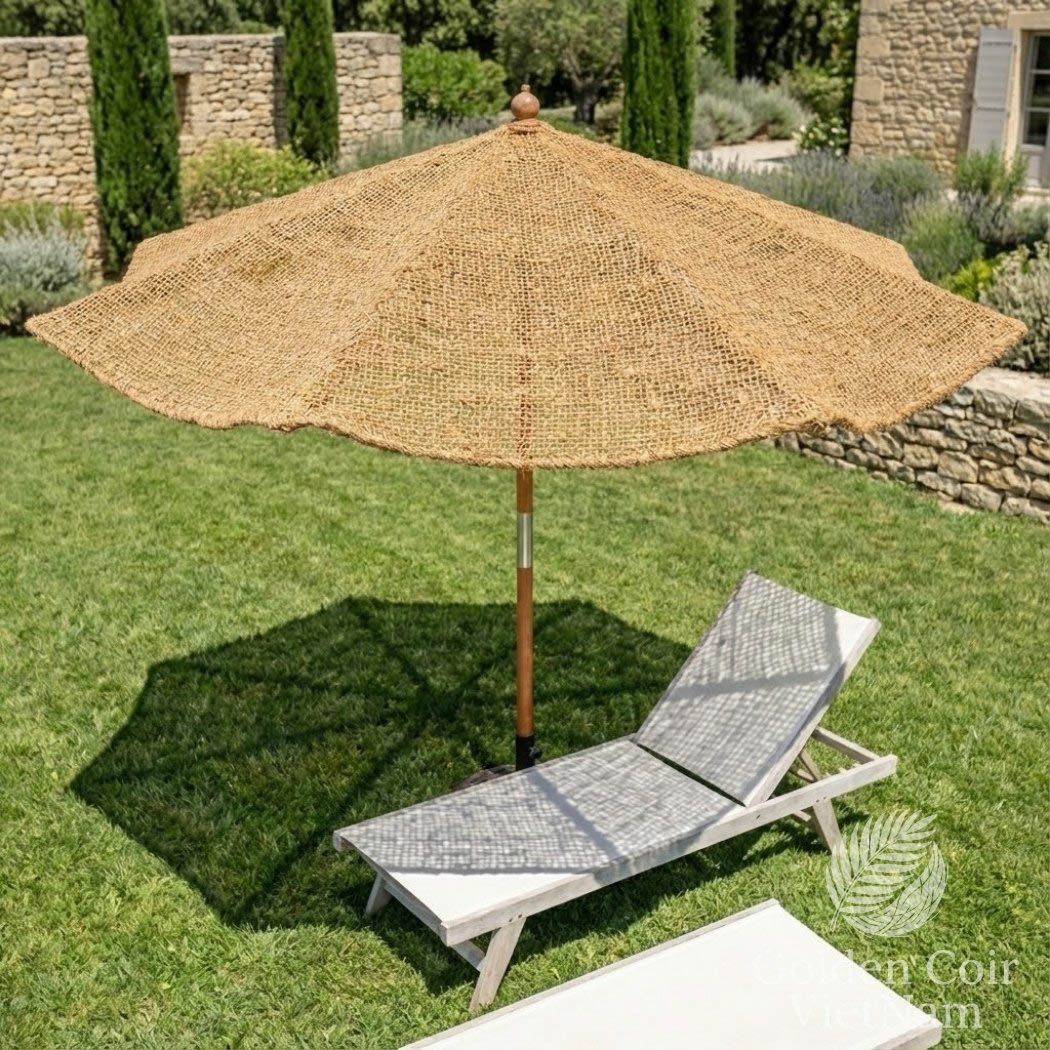 Patio umbrella and lounge chair on grass with stone wall and trees in the background