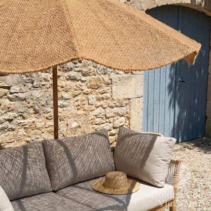 Outdoor seating area with a thatched umbrella, stone wall, and blue door.
