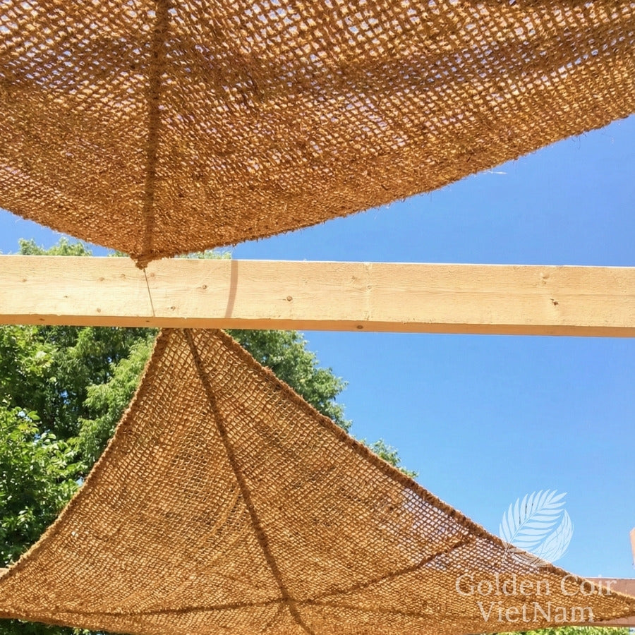 Woven canopy structure with wooden beams against a blue sky and green trees
